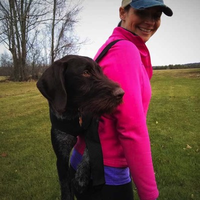 Woman uses mountain dog ware harness with her dog carried in it on her back 